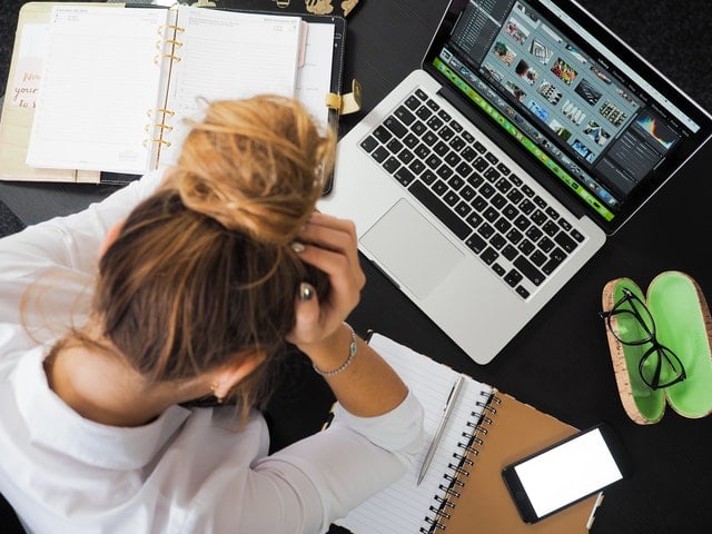 Woman holding her head facing desk